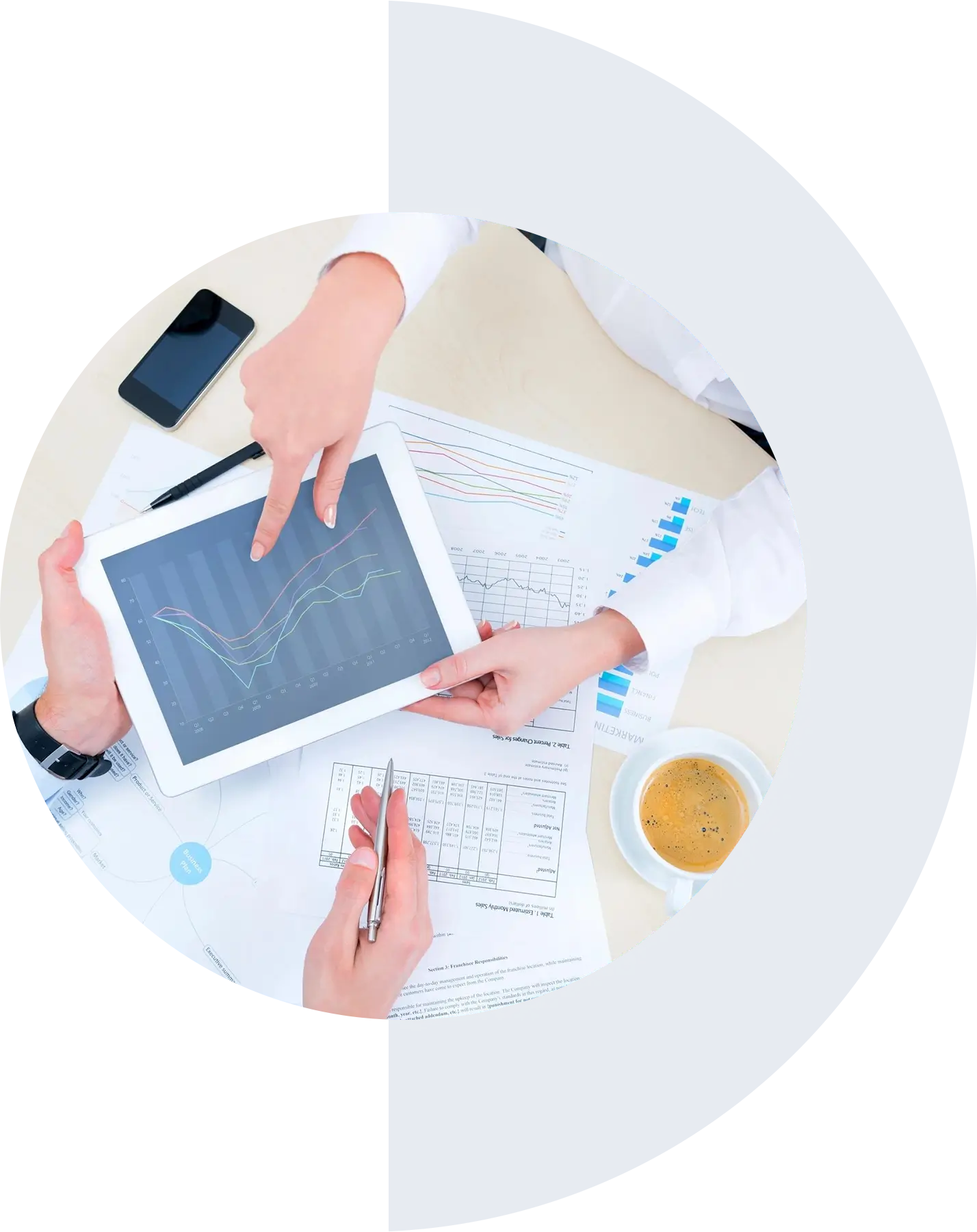 Two people review data on a tablet, surrounded by charts and graphs on paper. A cup of coffee, a pen, and a smartphone are also on the table.