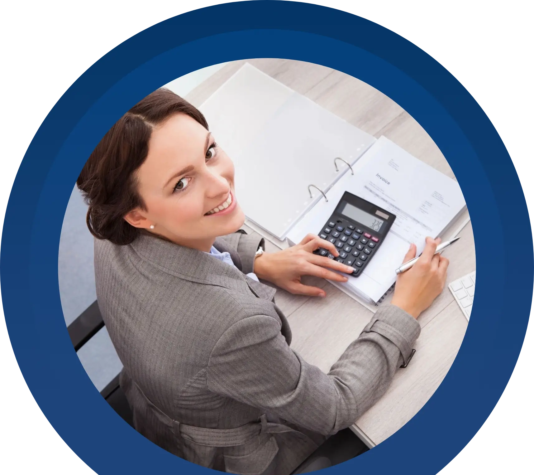 A woman in business attire smiles at the camera while using a calculator and writing in a binder at a desk.