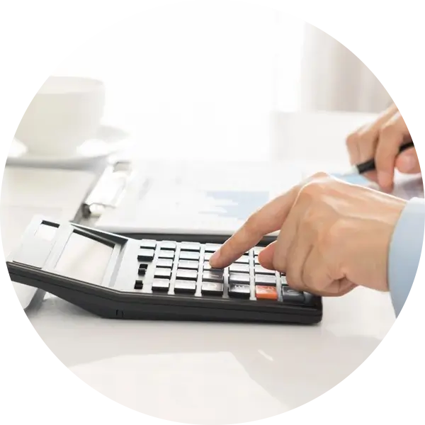 A person's hand is pressing buttons on a calculator, with a clipboard and a cup in the background.